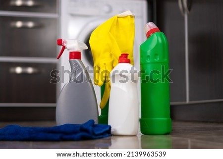 Close-up of bottles of cleaning products, a rag, yellow rubber gloves standing on the kitchen floor against the background of a washing machine. Concept of cleaning, household chores