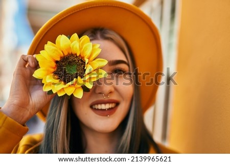 Young caucasian girl smiling happy holding sunflower over eye at the city.