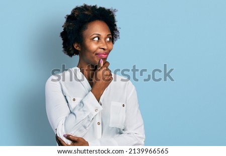 African american woman with afro hair wearing casual white t shirt with hand on chin thinking about question, pensive expression. smiling with thoughtful face. doubt concept. 