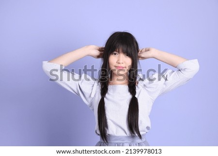 The young Asian girl in purple preppy dressed standing on the purple background.