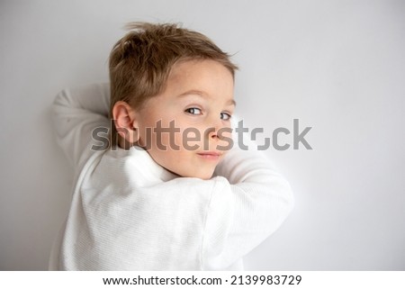 Cute stylish toddler child and older brother, boys with white shirts on white background, family kids portrait, studio shot
