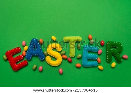 Handmade stuffed colorful felt letters on a green background. The concept of Easter. Minimalist creative. Poster or greeting card.