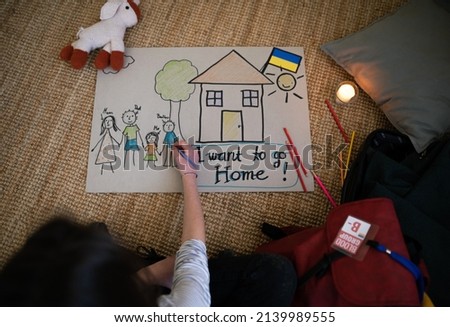 Top view of Ukrainian refugee schoolgirl missing home and drawing her family. Ukrainian war concept.
