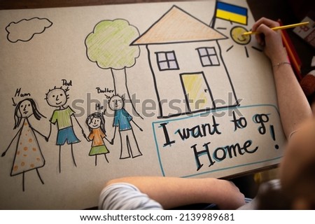 Top view of Ukrainian refugee schoolgirl missing home and drawing her family. Ukrainian war concept.