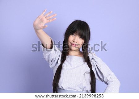 The young Asian girl in purple preppy dressed standing on the purple background.