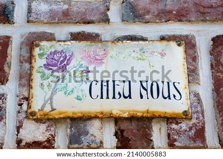 Vintage enamel sign on Norman brick wall inscribed "Chez Nous" in French Translation: With Us