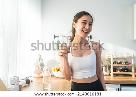Asian beautiful woman in sportswear drink water after exercise at home. Young thirsty active sport girl takes a sips of clean mineral natural in cup after workout for health care in kitchen in house. Royalty-Free Stock Photo #2140016181
