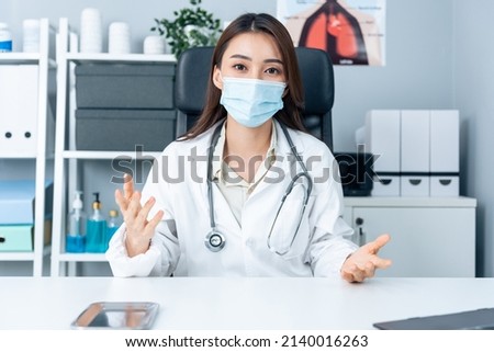 Asian young female medical doctor talking virtual online with patient. Attractive physician woman wear face mask, remote work from office hospital and broadcast diagnosis treatment to the sick people. Royalty-Free Stock Photo #2140016263