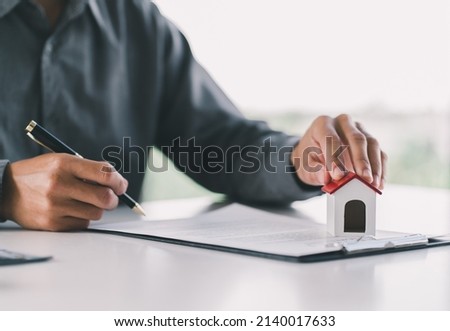 Close up wooden toy house with man signs a purchase contract or mortgage for a home, Real estate concept.