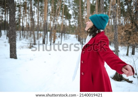 Beautiful smiling dark-haired woman in warm clothes enjoying cool winter weather while standing in a snow covered nature Royalty-Free Stock Photo #2140019421