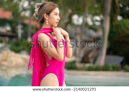 Woman in pink one piece swimsuit standing by swimming pool.