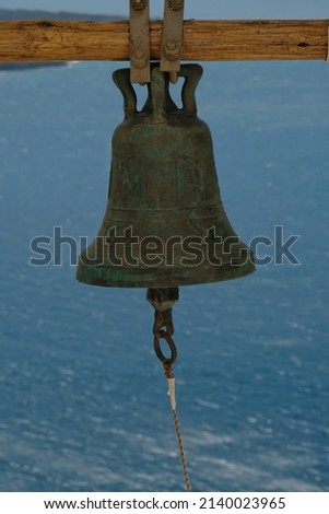 Closeup of a traditional church bell hanging from a wooden pilar and the aegean sea in the background in Santorini