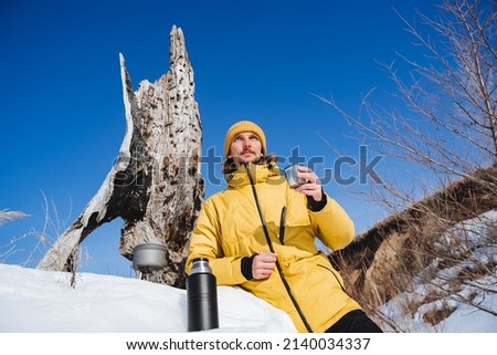 Drink tea from a thermos in nature in winter, a winter hike in sunny weather, yellow tourist clothes, a down jacket, a thermos with tea, hold a mug of coffee in your hand. High quality photo