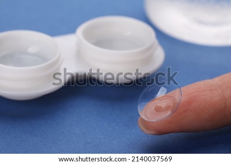 Woman with contact lens near case on blue background, closeup