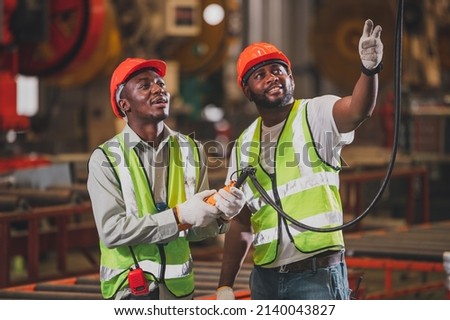 Two people black man African American worker control heavy machine in the factory.