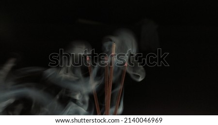 Group of red aromatic agarbathi, agarbatti or Incense sticks smoldering in room with smoke and aroma. Isolated in dark black background with copy space. It used in religious prayer. Closeup side view. Royalty-Free Stock Photo #2140046969