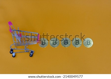 Small shoping cart with gold bitcoin arrang on orange background, Cryptocurrency shopping list concept.