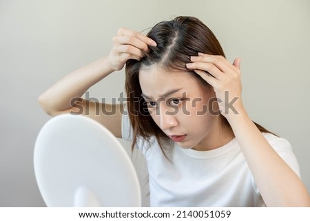 Damaged Hair, face serious asian young woman worry looking at scalp in mirror, hand in break into front hair loss, thin problem symptom at home. Health care shampoo beauty, isolated on background. Royalty-Free Stock Photo #2140051059