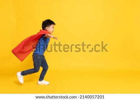 Superhero Asian boy in red cape running isolated yellow background, Full body composition Royalty-Free Stock Photo #2140057201