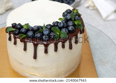 The creamy white cake is decorated with chocolate with blueberries on top. Place for the inscription. Image for website about food, confectionery. Selective focus.