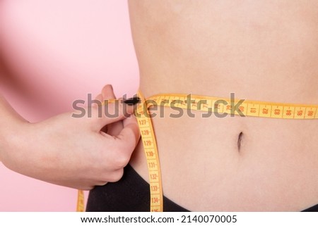 Slim woman measuring her waist's size with tape measure. Woman in great shape, perfect body shape. Torso of slim female. Close up Royalty-Free Stock Photo #2140070005