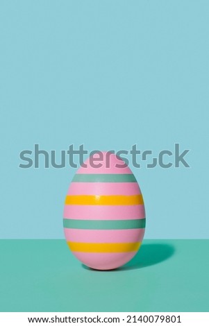 Pink striped Easter egg in 80s-90s retro style. A pink egg with multi-colored stripes on a two-tone background of mint and blue hues. Happy Easter vintage card. Royalty-Free Stock Photo #2140079801