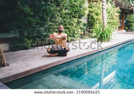 Portrait of Caucasian IT professional stretching hands while doing distance job - creating graphic design for web startup project, millennial male programmer with netbook posing at pool terrace