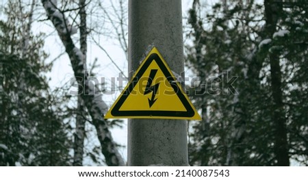 Yellow high voltage sign on a pole in the forest