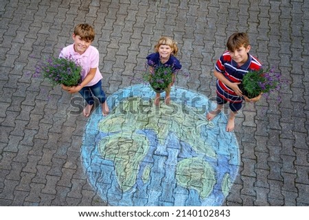 Little preschool girl and two school kids boys with flowers on earth globe painting with colorful chalks on ground. Happy earth day concept. Creation of children for saving world, environment peace.