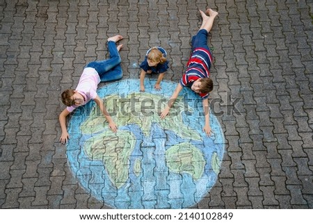 Little preschool girl and two school kids boys with earth globe painting with colorful chalks on ground. Happy earth day concept. Creation of children for saving world, environment and peace