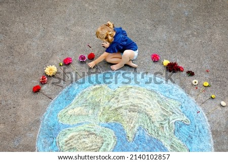 Little preschool girl with flowers and earth globe painting with colorful chalks on ground. Positive toddler child. Happy peace day concept. Creation of children for saving world, environment