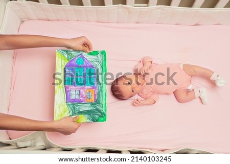 View from above of a little baby girl in pink and brother show in hands his drawing