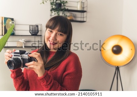 Young freelance creator at her studio. Cheerful caucasian woman holding her camera during photoshoot. High quality photo