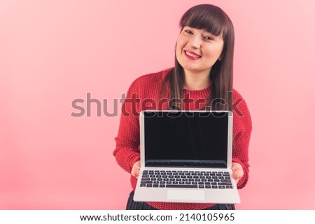 Smiling beautiful caucasian woman showing laptop with black mock-up screen to the camera over pink background. High quality photo
