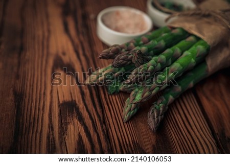 closeup picture of fresh sparrow grass ready to be cooked with salt and pepper on top of a textured wooden chopping board