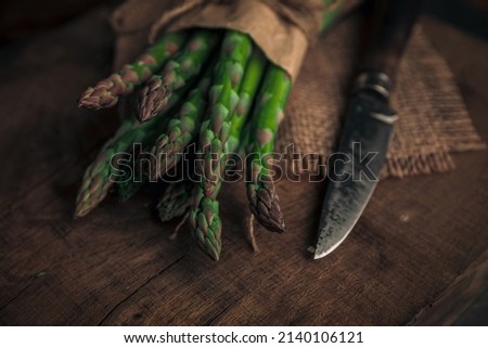 closeup picture of a sparrow grass's tip tied with rope on a cloth next to a knife ready for cooking on a chopping board