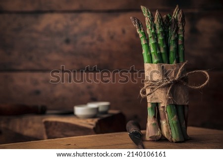 bunch of sparrow grass on top of a chopping board and a knife for chopping each and one of them in a rustic picture