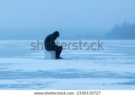 A fisherman on winter fishing on a frosty evening sits on an ice floe, in the fog, a winter landscape Royalty-Free Stock Photo #2140110727