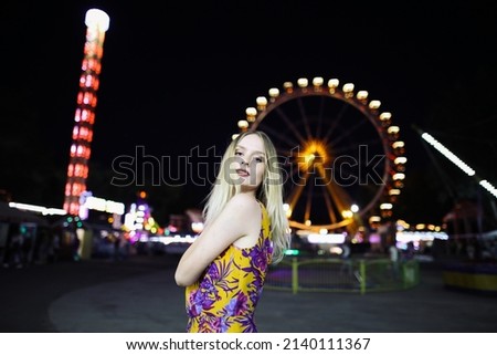 Girl at night in an amusement park against the backdrop of a ferris wheel. High quality photo