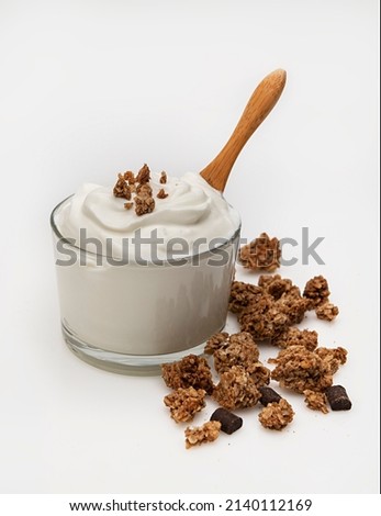 a bowl of greek yogurt with dark chocolate granola on a white background.A rustic spoon is in it as well, ready to serve.