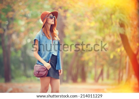 Redhead girl in sunglasses and hat in the autumn park.