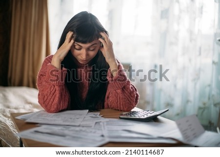 Sad woman holding her head over utility bills. The concept of rising prices for heating, gas, electricity. A young worried dissatisfied girl looks at papers does not expect a high cost of services Royalty-Free Stock Photo #2140114687