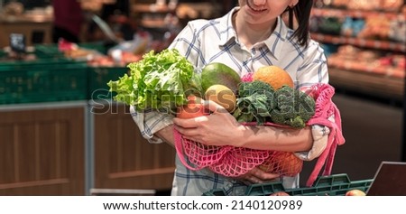 Young woman in a supermarket with vegetables and fruits, buying groceries.
