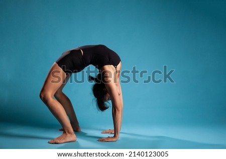 Athletic active person standing in bridge position training body endurance working at healthy lifestyle in studio with blue background. Personal trainer exercising posture
