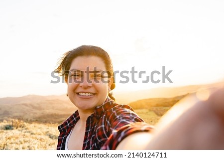 Beautiful Caucasian woman taking a selfie on the mountain very happy with a beautiful sunset.
