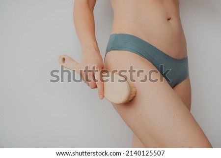 Woman's arm holding dry brush to top of her leg, cellulite treatment and dry brush. High quality photo