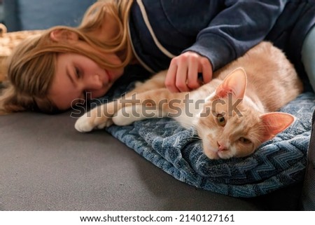 An Young Adolescent girl lying on a couch finds comfort by snuggling close to and petting her cat Royalty-Free Stock Photo #2140127161