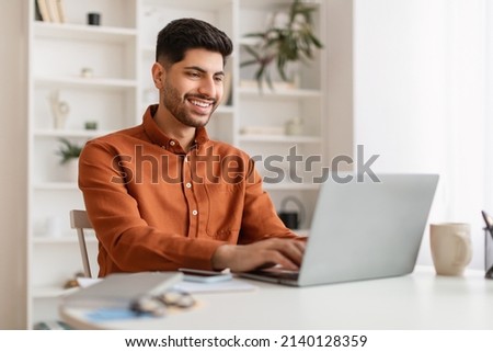 Portrait Of Smiling Middle Eastern Male Manager Working On Laptop Computer In Modern Office, Cheerful Guy Sitting At Desk And Using Pc, Looking At Screen Typing On Keyboard, Enjoying Remote Job Royalty-Free Stock Photo #2140128359
