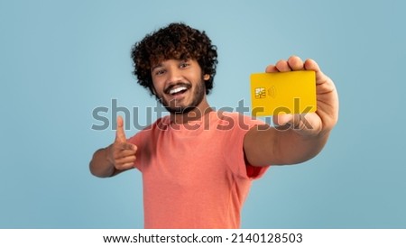 Cheerful handsome young indian man holding yellow credit card and showing thumb up, pleased client demonstrating bank product over blue studio background, panorama. Finance, loan, savings concept Royalty-Free Stock Photo #2140128503