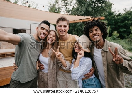 Silly young diverse friends posing near camper van in countryside, making different gestures, taking selfie on camping trip. Cheerful millennial people spending summer holidays in nature
